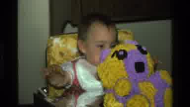 California USA (1977): A Baby Sitting On Chair Holding A Teddy-Bear With Watery