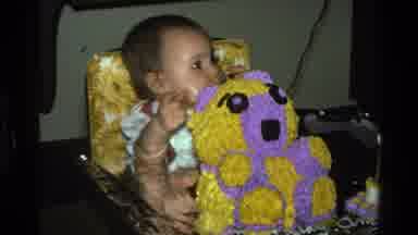 California USA (1977): Baby Sits In Yellow High Chair Eating Purple And Yellow