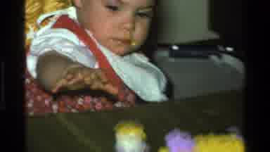 California USA (1977): Baby Wearing Red Dress Reaches For White Toy Sitting On