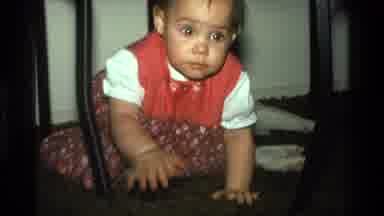 California USA (1977): Baby Wearing Red And White Overalls Crawls Through Brown