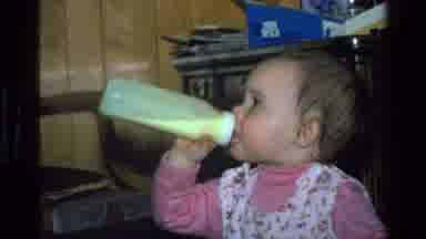 California USA (1977): Baby Drinking From Bottle And Walking Around Dad In Chair