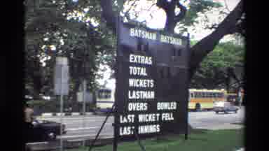 Singapore (1984): A Sports Scoreboard Sits On Grass Under A Tree Next To An Urban