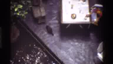 Thailand (1984): Driving In Vehicles In Busy Area Passing Sign That Reads Akai