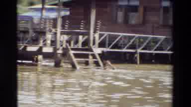 Thailand (1984): There Are People Swimming In The Water Next To Some Buildings