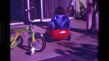 California USA (1979): Little Girl In Blue Jacket Riding Around In Red Toy Getting