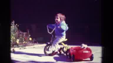 California USA (1979): A Boy Riding A Bicycle Pulling A Wagon Containing A Doll