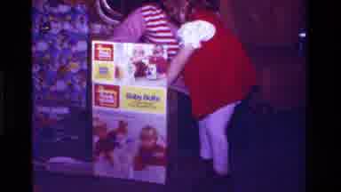 California USA (1979): Toddler Excitedly Opening Toy Xmas Gift With Older Woman