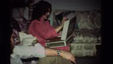 California USA (1981): Excited Young Woman In Pink Giddily Opens Up A Gift Box