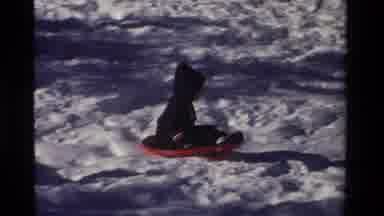 California USA (1981): Child Wearing Coat Sledding Down Snowy Slope On Sunny