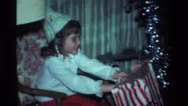 California USA (1984): Young Girl Sitting On Chair Opening Wrapped Gift Excited