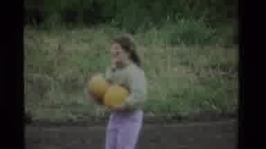California USA (1984): Female Carrying Two Orange Pumpkins While Wearing Purple