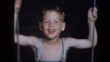 New York USA (1939): Young Boy Smiling Swinging On A Swing Wearing Denim Overalls