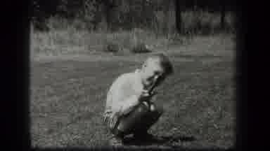 New York USA (1939): Boy Squatting On Lawn Pointing A Toy Or Stick At The Camera