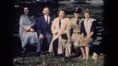 New York USA (1959): Five Smiling People Sitting On Park Bench On A Windy Day In