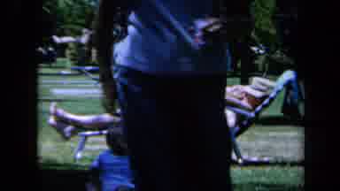 California USA (1961): Man Sitting In Lawn Chair At A Park Smoking While Kids Play