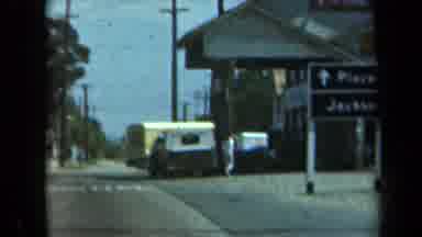 California USA (1969): Driving Down Road With Person Walking Up To Store Front