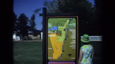California USA (1971): Woman In Green Hat Looking At Park Map Near Grass And Pond