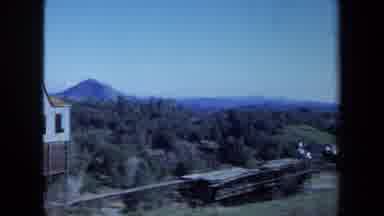 Maine USA (1971): Woman Standing On A Big White Porch Overlooking Buildings And