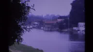 London England (1969): A View Of Homes Built And Three People Along The Riverbank