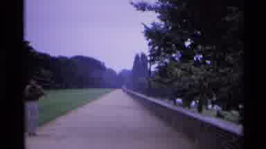 London England (1969): A Man Picks Up An Object From A Large Walkway Bordered By A