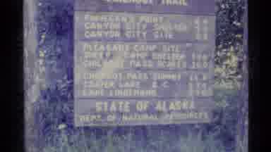 Alaska USA (1977): A Sign From Alaska And Two People Walking With Things On Their