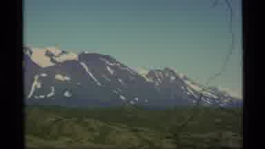 Alaska USA (1977): A View Of Green Grass With Snow Capped Mountains In The