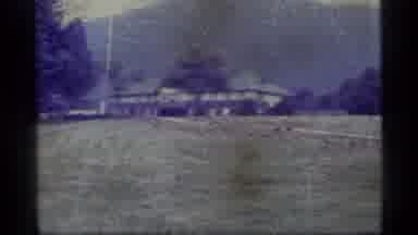Alaska USA (1977): Duck Walks Across Grass In Front Of Brown Farm Buildings