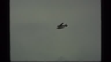 Alaska USA (1977): High In The Sky A Plane Flies Over A Boat Sailing Across The
