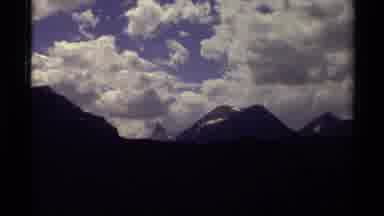 Canada (1979): Panning View Of Tall Mountains And White Fluffy Clouds Blue Sky