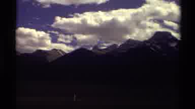 Canada (1979): Tall Mountains Line The Road As Cars Zip By Under The Blue Sky