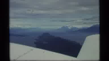 Alaska USA (1977): Airplane Flying In Cloudy Skies Over Many Snow Filled Mountains