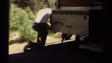 Mendocino California USA (1980): Man Fixing Camping Vehicle Wheels And Reading A
