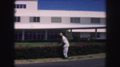 KANSAS CITY MISSOURI-1959: Man Trims Hedge With Red Blooming Flowers Next To White Building