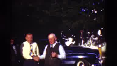 Denmark (1975): Two Men Wearing Shirts And Ties Shake Hands In Front Of Blue Car
