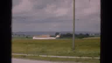 Denmark (1975): View Of Green Field With Tan Structure On A Clear Sunny Day