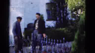 DENMARK-1975: Two Men Speak Near Iron Fence In Front Of White Brick Building
