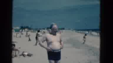 Florida USA (1975): Older Gentleman In Black Swim Trunks Walking On A Sandy Beach