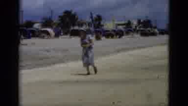 Florida USA (1975): Woman Wearing Blue Dress And Hat Walking On Beach On A Bright