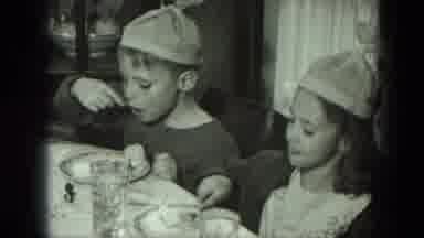 West Germany (1951): Young Children All Wearing Silly Hats Sitting At A Kitchen
