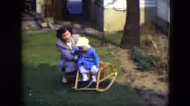 Cleveland Ohio (1951): Woman Helps Baby Wearing Blue Coat Sit In Small Rocking