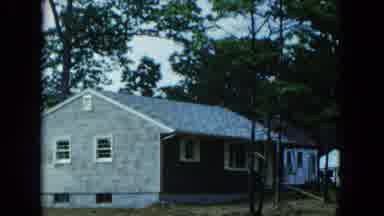 Hicksville New York (1954): Blue Car Parked Next To Grey Building On A Cloudy Day