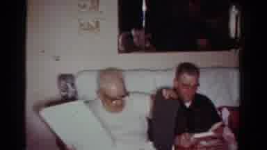 Toledo Ohio USA (1954): Man Wearing Glasses Unwraps Gift While Person Removes Snow