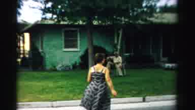 Normal Illinois USA (1957): Woman In Dress Walks Across Street To Man Sitting In