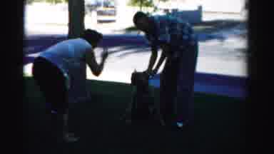 Nevada USA (1957): Woman Wearing Black Shorts Scolds Dog While Man Rubs Dog's Head
