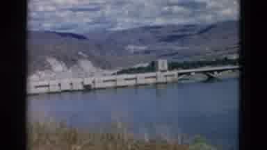 Montana USA (1958): Vehicles Travel On A Bridge On A Quiet Body Of Water Under A