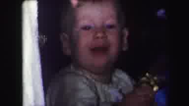 Lynbrook New York (1971): Happy Baby Holding Up A Golden Toy As A Toddler Walks In