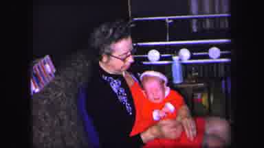 Lynbrook New York (1971): Woman Wearing Blue Sweater Holds Baby Wearing A Red