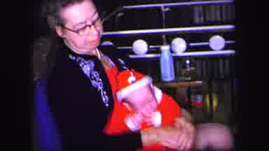 Lynbrook New York (1971): Woman Wearing Blue Sweater Holds Baby Wearing Red Santa