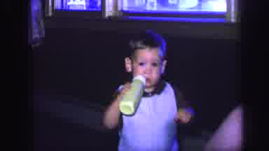Lynbrook New York (1971): A Toddler Sipping On His Bottle As Another Child Pops Up