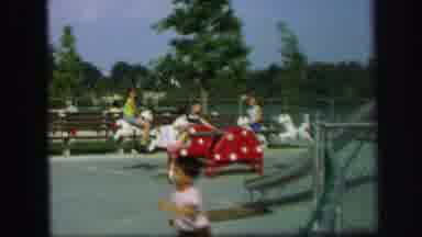 Lynbrook New York (1971): Baby Wearing White Shirt Watches Kids Play On Seesaw On
